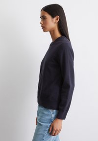 Marineblauwe trui met ronde hals in een zachte brei, met lange mouwen en geribbelde manchetten, gecombineerd met lichtblauwe spijkerbroeken. Soepele textuur.