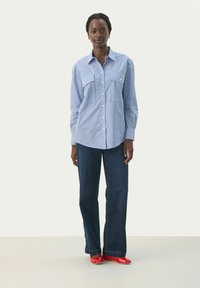 Striped, light blue button-up shirt with two chest pockets, paired with dark blue wide-leg jeans and red shoes. Smooth texture; casual design.