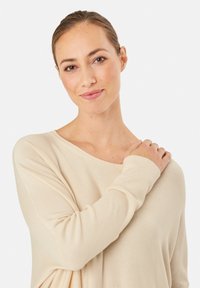 Cremfarbener, übergroßer Pullover mit gerippter Textur, weitem Ausschnitt und langen Ärmeln. Weiches Material mit minimalistischem Design.