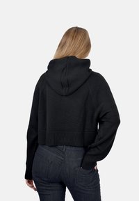 Felpa nera cropped in tessuto a maglia, con cappuccio, orlo a costine e maniche lunghe. La vista posteriore mostra i dettagli di design e tessuto.