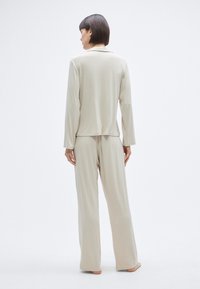 Σετ άνετης ρούχων σε ανοιχτό μπεζ χρώμα με μακρυμάνικη μπλούζα με γιακά και παντελόνι φαρδιάς γραμμής. Μαλακό, υφασμένο ύφασμα με άνετη εφαρμογή.