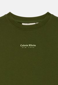 Olivenfarget crewneck genser med ribbet krage og sentrert Calvin Klein New York-logo i lysegrønn skrift.