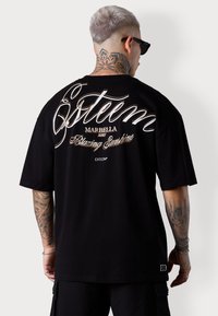 Schwarzes, übergroßes T-Shirt mit schriftartähnlichem Text auf dem Rücken, einschließlich Logos und Designdetails, aus weichem Stoff gefertigt.