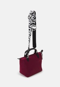 Červená látková taška s černými koženými doplňky, horními rukojeťmi a odnímateln ým ramenním popruhem s výrazným bílým textovým vzorem. Zavírání na zip.