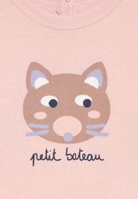 Šviesiai rožinė medžiaga su spausdintu katės veidu rudais atspalviais, baltais ir mėlynais akcentais, o apačioje yra tekstas "petit bateau".