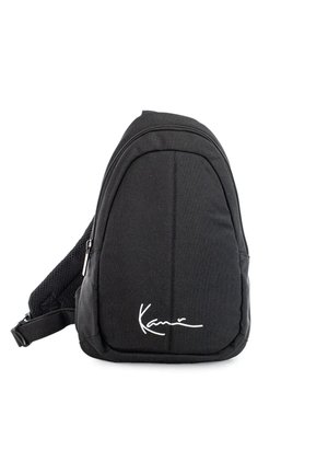 Kompaktowy czarny plecak na jedno ramię z przednią kieszenią na suwak i białym, kursywnym logo w dolnym środku.