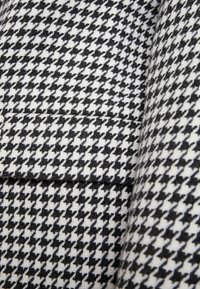 Tessuto a motivo houndstooth in bianco e nero; trama texture; presenta una leggera lucentezza; lavorato a maglia stretta con un aspetto strutturato.