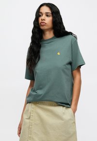 Πράσινη βαμβακερή μπλούζα με κοντά μανίκια, διαθέτει ένα μικρό κίτρινο λογότυπο στο στήθος. Μαλακή υφή με άνετη εφαρμογή.