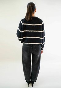 Pull en tricot à rayures noires et blanches, design court, associé à un jean noir ample et des escarpins noirs.