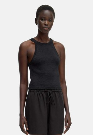 Schwarzes, gestricktes Tanktop mit hohem Ausschnitt, offenen Schultern und strukturiertem Stoff, kombiniert mit lockeren schwarzen Shorts.