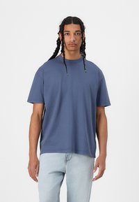 T-shirt azul de manga curta com gola redonda, feito de algodão. Apresenta um corte descontraído e uma textura suave. Combinado com jeans azul-claro.
