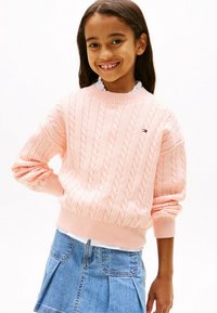 Rosa Kabelstrickpullover mit gerippten Bündchen und Saum, kombiniert mit einem hellen Jeansrock mit Taschen und Falten.