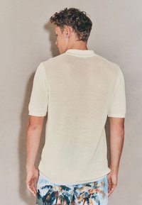 Polo en mesh jaune clair à manches courtes, avec un col classique, coupe ample, accompagné d'un short de bain contrastant arborant un motif de palmiers.