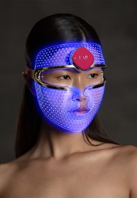 LED facial mask in blue with a transparent, dotted surface and a pink control panel. Features a snug design and gold accents.
