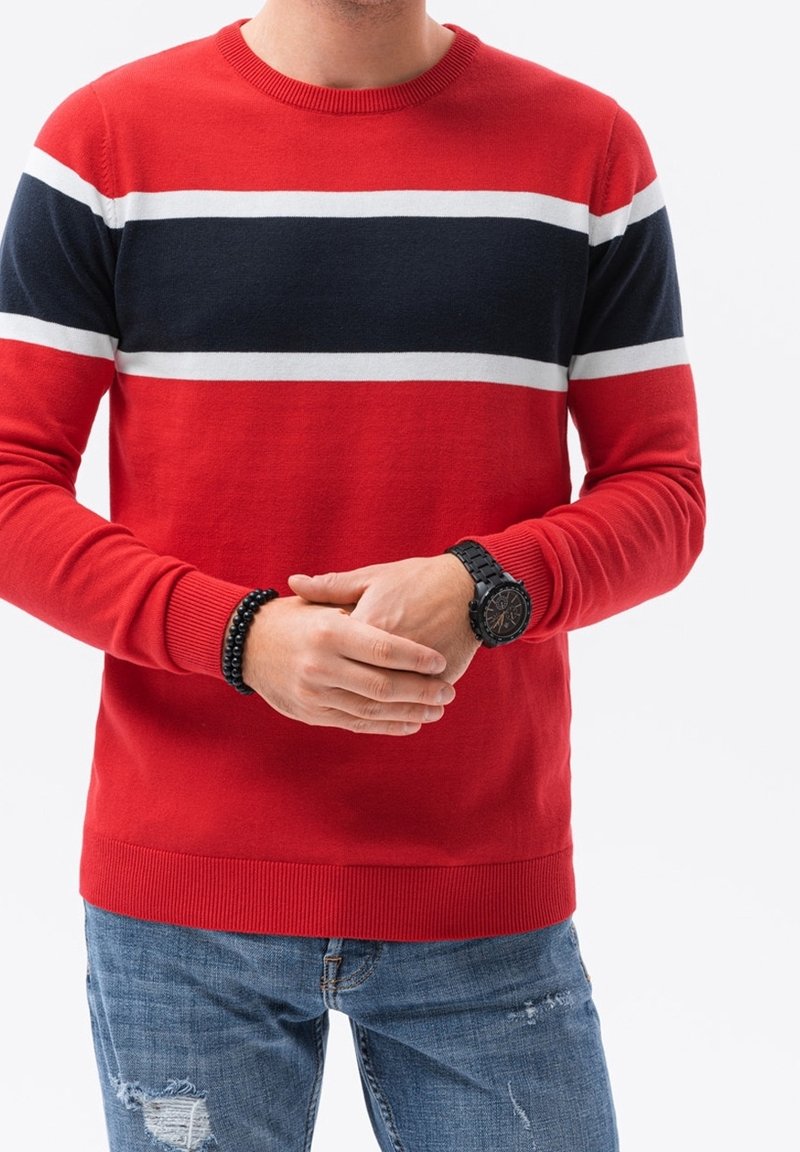 Rode gebreide trui met marineblauwe en witte horizontale strepen. Geribde halslijn en manchetten, gecombineerd met versleten blauwe spijkerbroek en een zwart horloge.