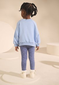 Sweat-shirt oversize bleu clair avec poignets côtelés, associé à des leggings bleus ornés de pois roses. Bottes blanches avec détails effilochés.