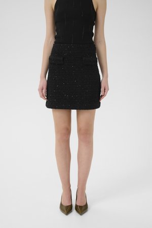 Sort tweed mini-skirt med tekstureret stof, to forlommer og en tætsiddende talje. Sættes sammen med en sort ærmeløs top og olivengrønne hæle.