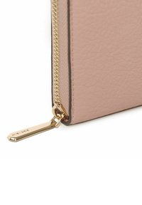 Angolo di una borsa in pelle texturizzata rosa con cerniera e accessori in oro. Il tirazip presenta un dettaglio di branding inciso.