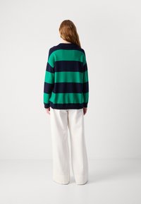 Gestreifter Pullover in Grün und Marineblau mit geripptem Kragen, lässiger Passform und leichtem Stoff, kombiniert mit weißen, weiten Hosen.