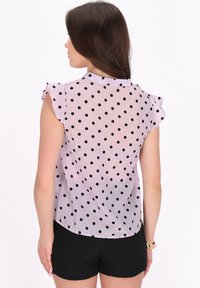 Lichtpaarse sheer blouse met zwarte stippen, korte fluttermouwen en een ronde zoom, gecombineerd met zwarte shorts.