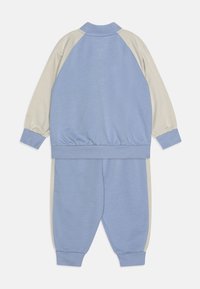 Dvodijelni trenirku koji se sastoji od bomber jakne u svijetloplavoj i krem boji, s elastičnim rukavima i strukom, uparen s odgovarajućim trenirkama.