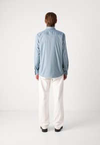 Cămașă albastră în dungi, cu mâneci lungi, guler și manșete cu nasturi, asortată cu pantaloni albi, lejeri și încălțăminte neagră.