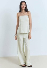 Top brez naramnic v svetlo zeleni tkanini, v kombinaciji s širokimi hlačami. Gladka tekstura, minimalistična zasnova, preprost silhuet, obut v ravne sandale.
