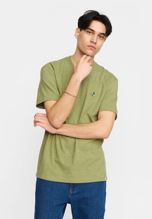 Olivengrøn bomulds t-shirt med korte ærmer, rund hals og en lille broderet detalje på brystet. Kombineret med blå denim jeans.