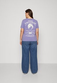 Purple graphic t-shirt featuring cosmic motifs: moon phases, a butterfly, and text. Loose-fitting denim jeans with a classic cut.