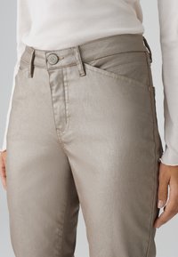 Pantalon taupe métallique avec une coupe slim, un léger éclat, un design à cinq poches, et une fermeture par bouton avec des détails de couture contrastés.