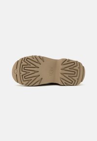Suola in gomma color tan con un motivo a zigzag per la trazione, con un logo circolare sul tallone e bordi testurizzati.