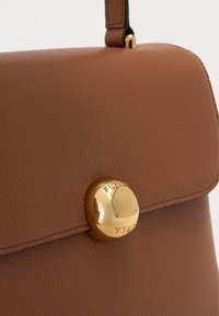 Brown textured leather bag with a round shiny gold clasp engraved with the brand name, and a matching leather strap attached.