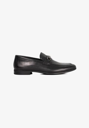 Black leather loafers with a round toe, flat heel, and a decorative metal buckle on the front. Smooth finish with subtle shine.