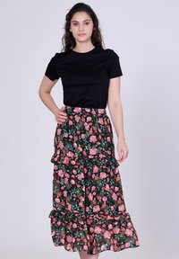 T-shirt noir à manches courtes associé à une jupe maxi fleurie avec une base noire, des roses roses, des feuilles vertes et des volants superposés à l'ourlet.