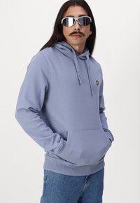 Felpa con cappuccio di colore lilla chiaro, con tasca a marsupio e polsini a costine. Presenta un piccolo logo giallo sul petto e una vestibilità comoda.