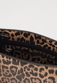 Taske med leopardprint, der har et glat, struktureret design med sorte detaljer og en indvendig lynlås-lomme. Teksturert mønster overalt.