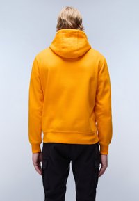 Geel hoodie met een kangoeroezak, ribbelmanchetten en zoom. Glad textuur; van achter gezien, gedragen met zwarte broek.