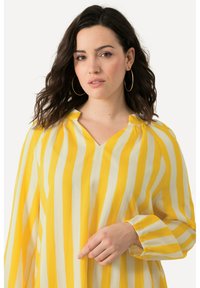Blusa a righe gialle e bianche con scollo a V, maniche lunghe e dettagli arricciati sulle spalle. Tessuto leggero e texturizzato.