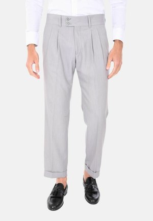 Pantaloni grigi con pieghe, dotati di una cintura con due bottoni, vestibilità su misura e orli risvoltati, abbinati a mocassini neri.