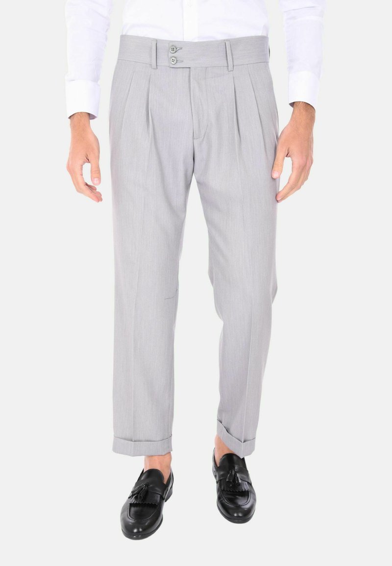 Pantaloni grigi con pieghe, dotati di una cintura con due bottoni, vestibilità su misura e orli risvoltati, abbinati a mocassini neri.