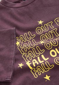 Violetti puuvillapaita, jossa on keltainen teksti "FALL OUT" rohkealla ja leikkisällä fontilla, sekä pieniä tähden korostuksia sanojen ympärillä.