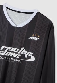 Maglietta da calcio nera con strisce verticali, colletto bianco e logo con tre stelle. Il testo include "rise the shine" e "FOOTBALL MOMENTS."