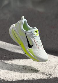 Λευκό παπούτσι τρεξίματος με υφασμάτινη επάνω επιφάνεια, μαύρο λογότυπο Nike, έντονες κίτρινες λεπτομέρειες και ανακλαστικά στοιχεία. Ελαφρύς σχεδιασμός για καλύτερη απόδοση.