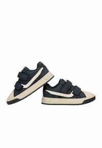 Baskets pour enfants noires et beiges avec des bandes blanches sur les côtés et deux bandes Velcro noires sur chaque chaussure.