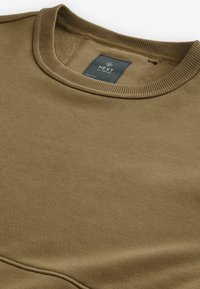Sudadera de algodón marrón con cuello redondo, ribetes acanalados y una etiqueta en el interior. Textura suave, diseño minimalista.