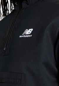 Chaqueta tipo pulóver negra con medio cierre y confeccionada en tela texturizada. Cuenta con un bolsillo frontal y un logo blanco bordado. Acabado liso.