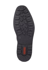 Semelle de chaussure en caoutchouc noire avec un motif de profil présentant des formes angulaires et des étoiles. Centre marqué d'un logo circulaire en rouge. Texture durable.