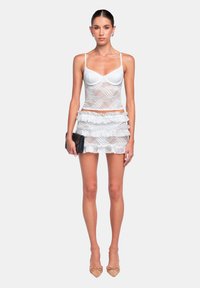 Top bianco in pizzo con spalline sottili e gonna mini a strati con volants. L'outfit presenta un design aderente e una texture trasparente. Accessorio clutch nero.