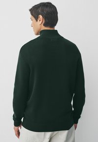 Dunkelgrüner Strickpullover mit hohem Kragen, gerippten Bündchen und Saum. Verfügt über einen strukturierten Stoff, der sich ideal für Schichten-Outfits eignet.