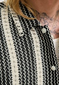 Chaqueta de tweed con un patrón de rayas en blanco y negro, con una tela texturizada, cuello puntiagudo y botones blancos en el frente.